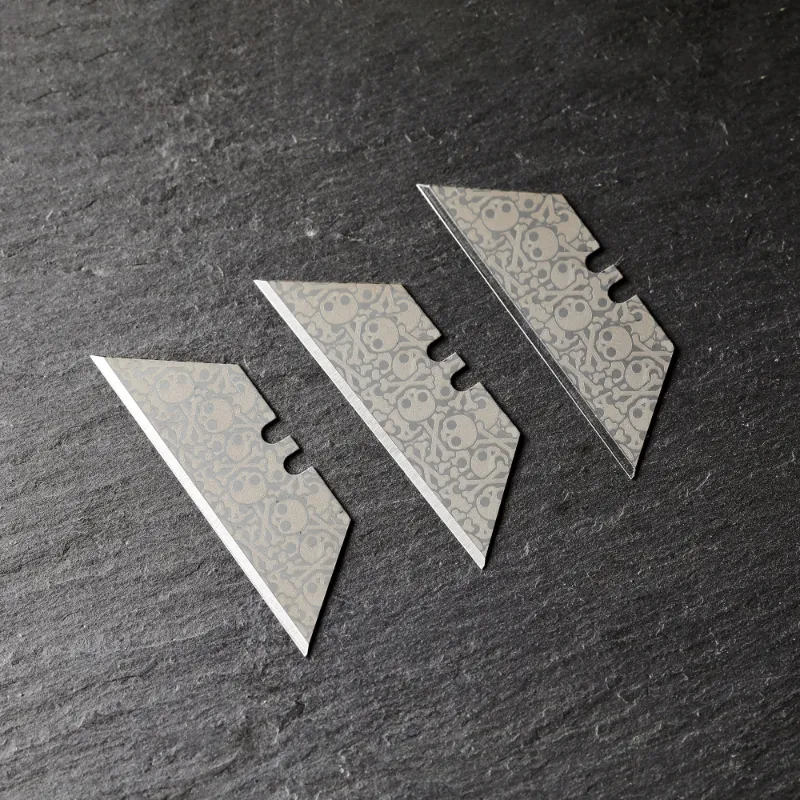The Stinger Tools laser engraved utility razor blades with skull pattern, three silver trapezoid blades